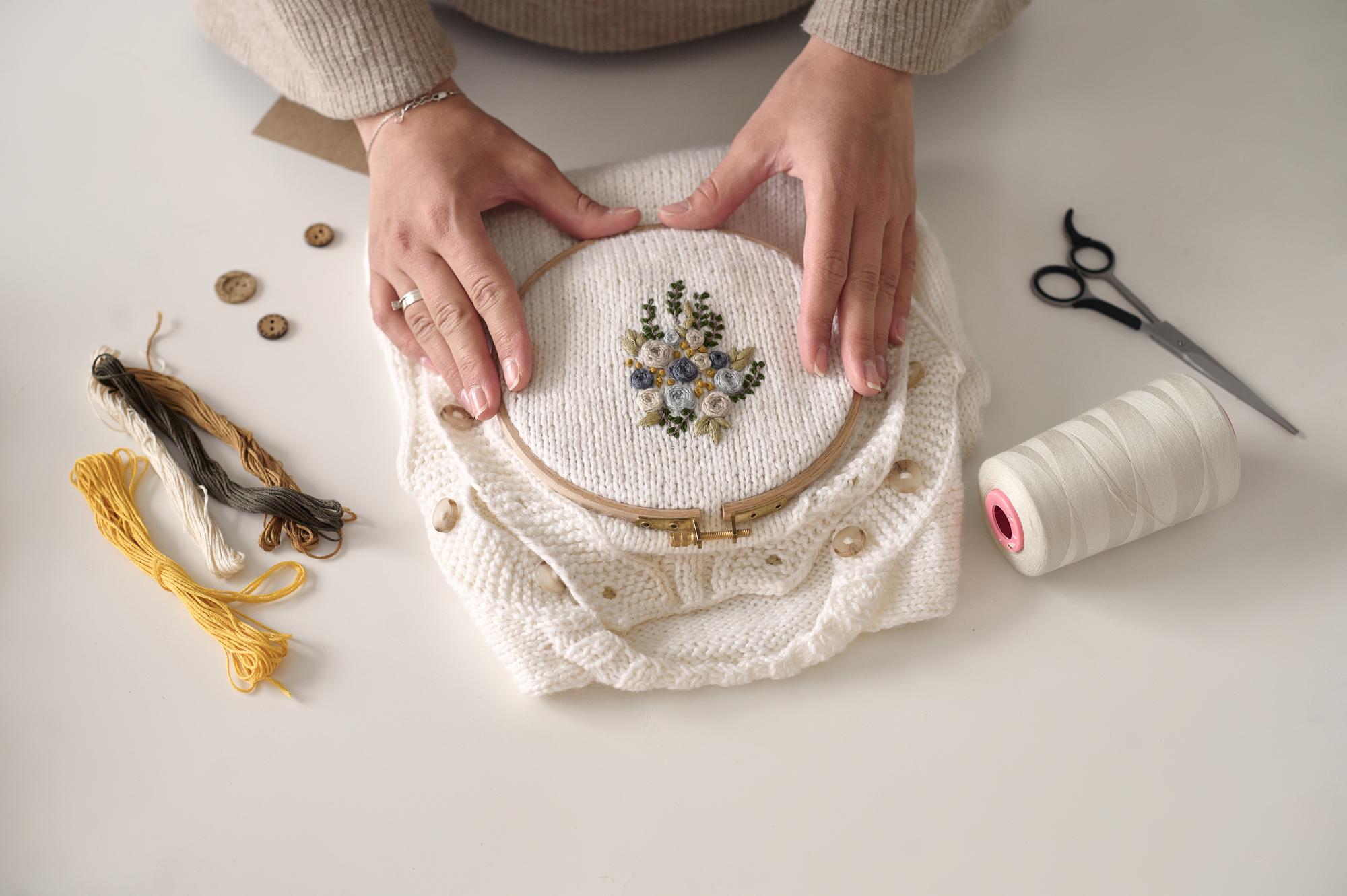 Detail of hands embroidering a floral motif on linen